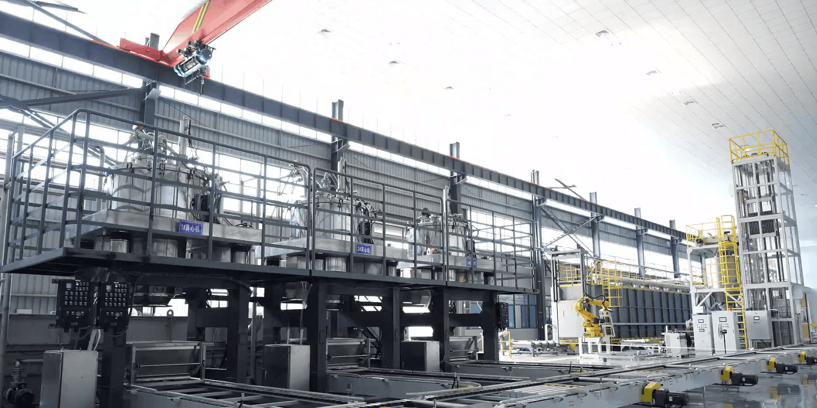 Factory floor with stainless centrifuge line, safety railings, and yellow robotic arm beside processing units.