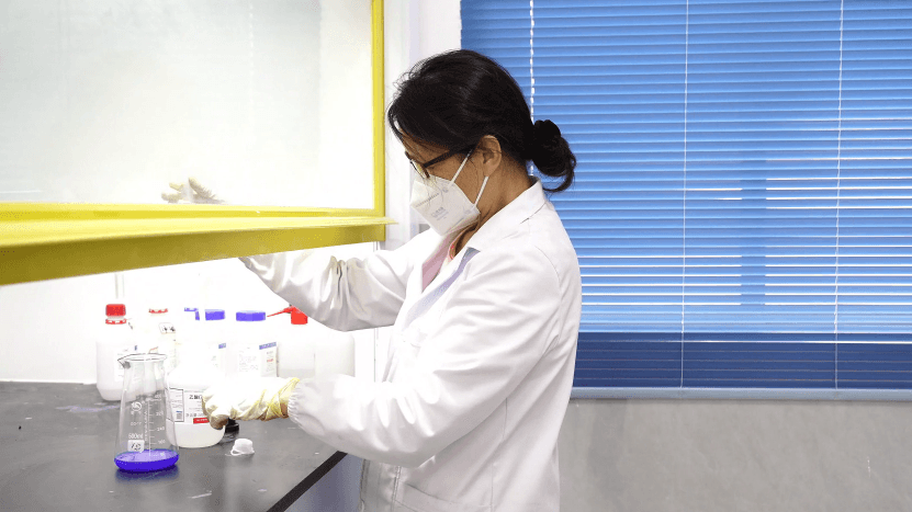 Laboratory technician performing titration with a burette and Erlenmeyer flask on the bench.