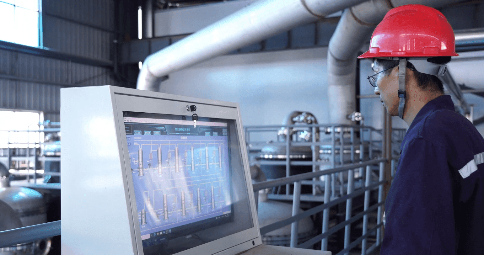 Operator in safety gear monitoring industrial process on a plant control screen.